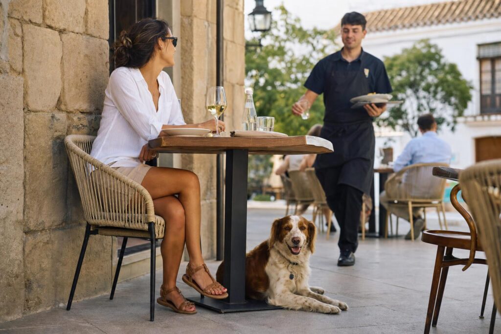Osoba z psem przy stoliku na tarasie restauracji w Hiszpanii.